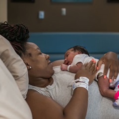 A woman rests in bed with her newborn baby moments after natural childbirth